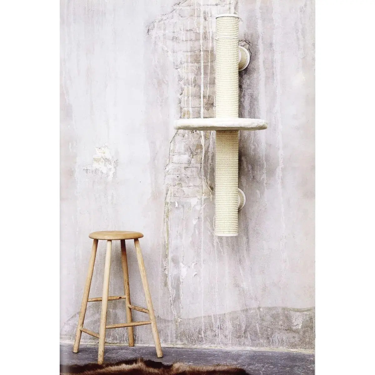 Stylish cat scratching post mounted on a wall beside a wooden stool in a minimalist interior.