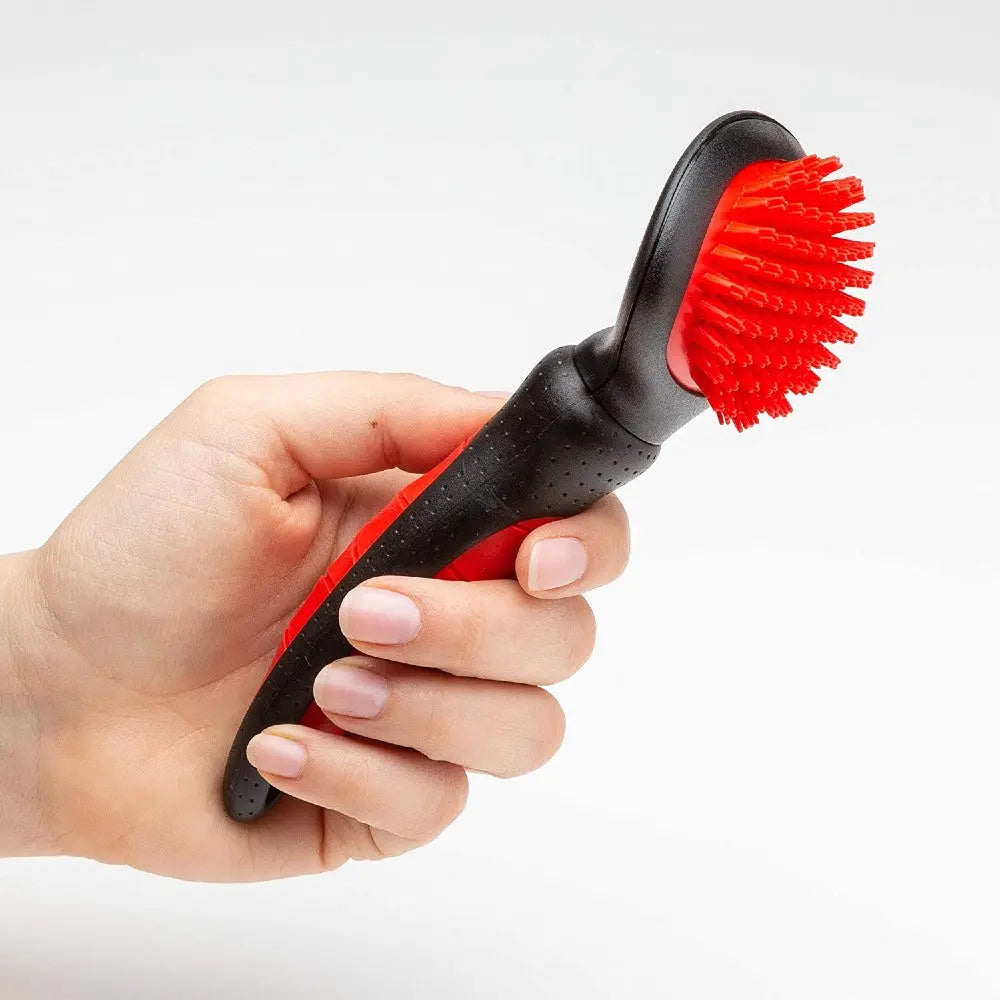 Hand holding a red and black pet grooming brush with rubber bristles for effective fur removal.