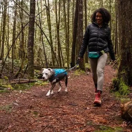 Woman walking a dog on a forest trail, enjoying nature and outdoor adventure together.