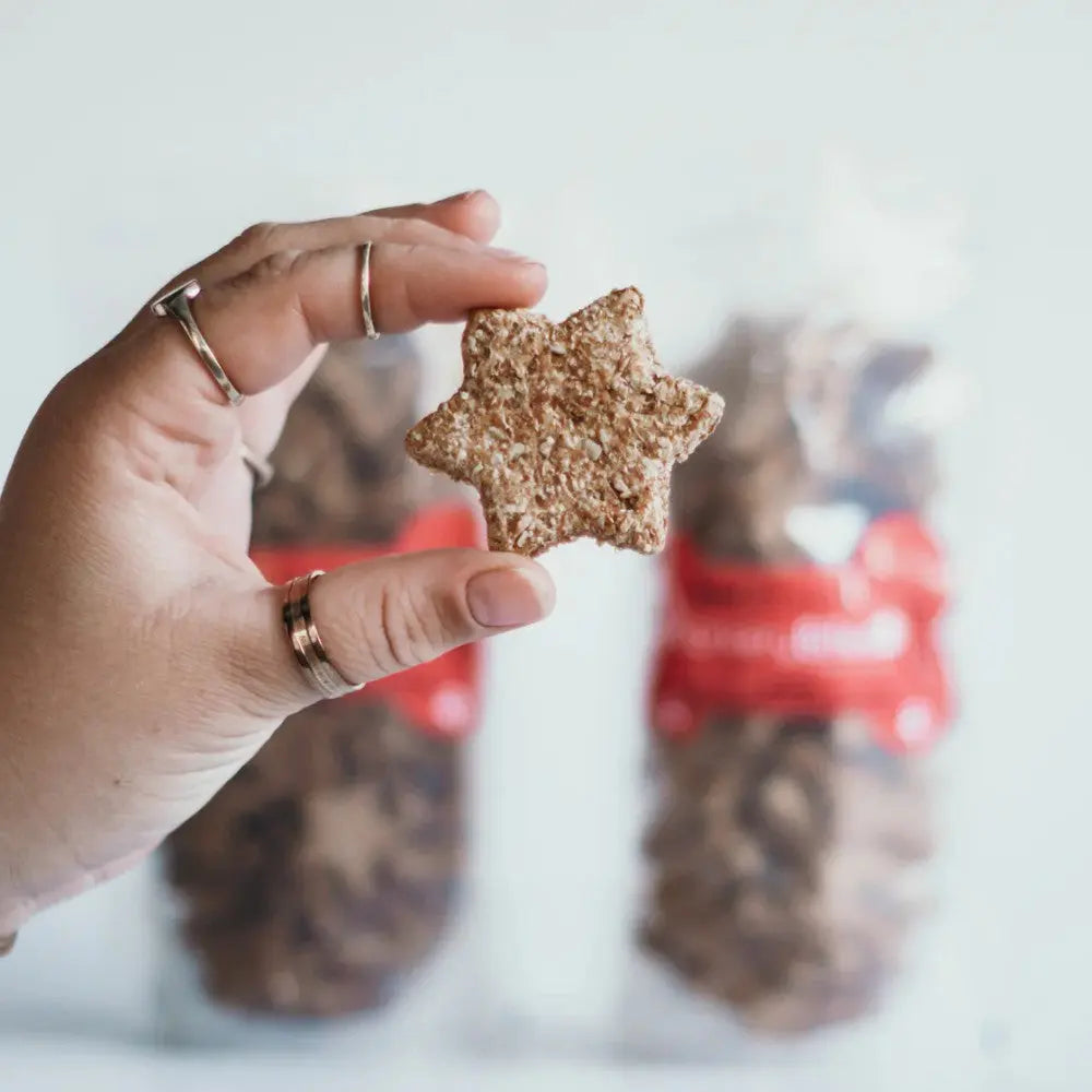 Hand holding a star-shaped cookie with packaged treats in the background.