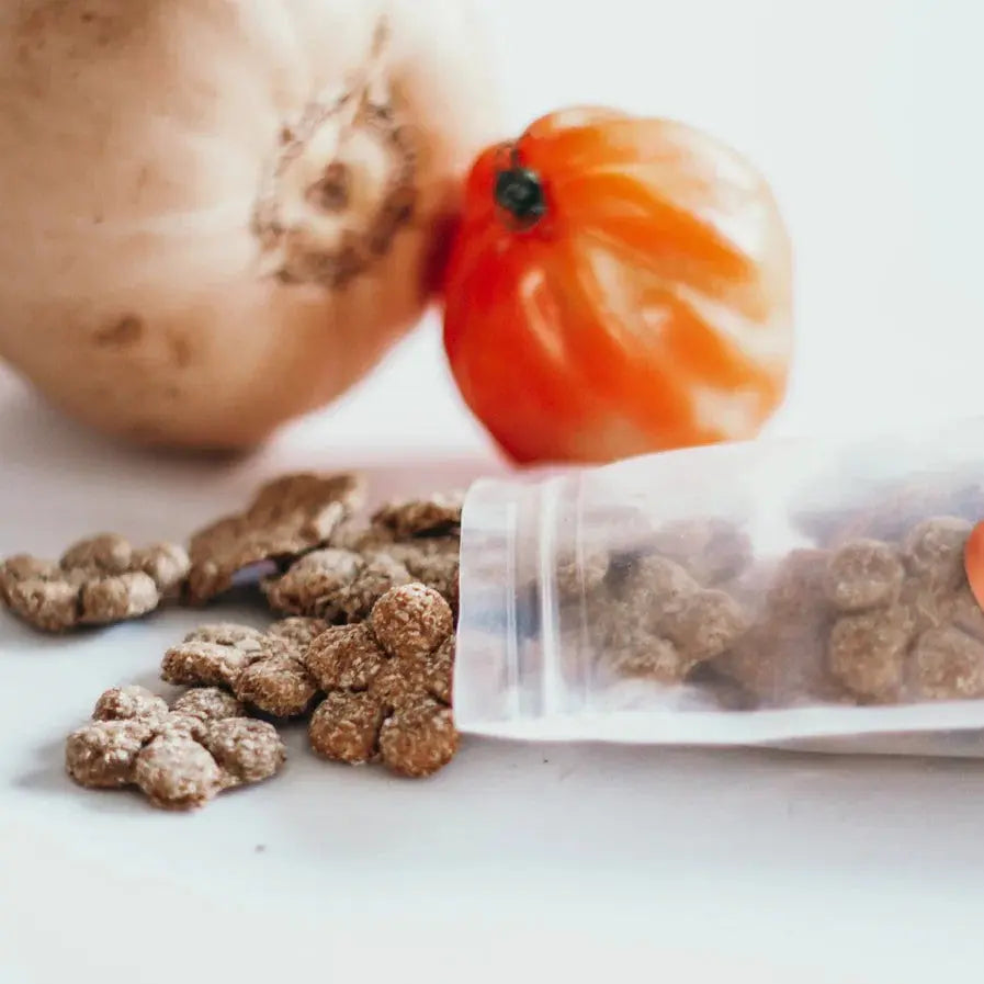 Pet food with natural ingredients, featuring a bag, vegetables, and kibble on a clean surface.