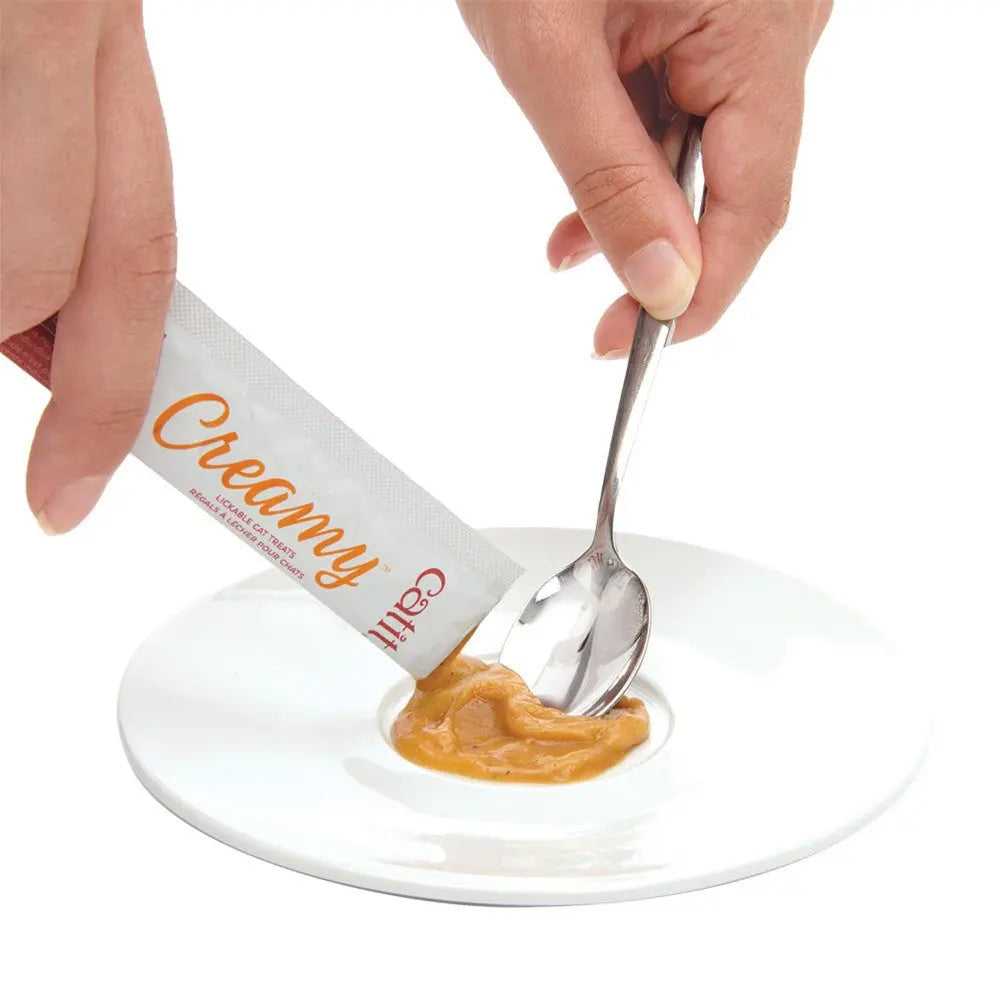 Hand squeezing creamy peanut butter from a pouch onto a white plate with a spoon.