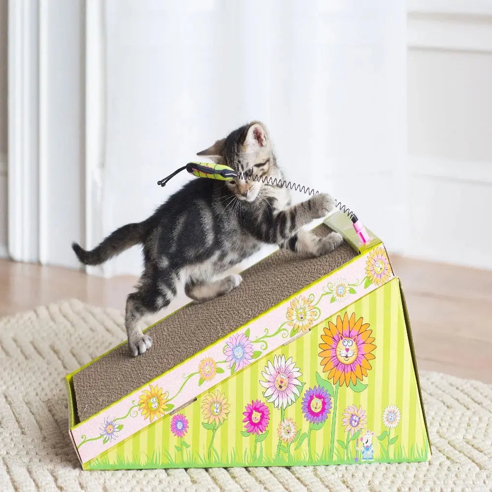 Playful kitten climbing a colorful flower-patterned scratching ramp.