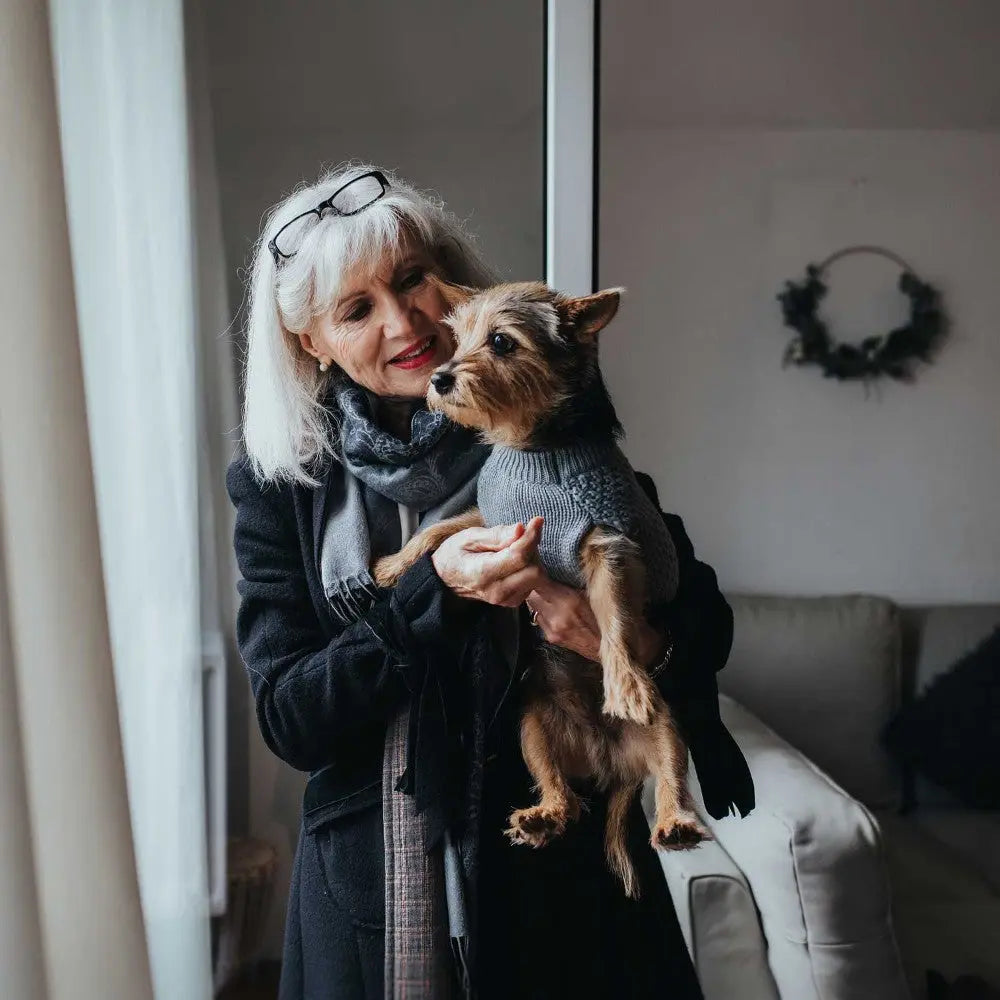 Woman holding a small dog in a cozy living room, both looking content and stylish.