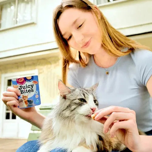 Woman feeding her cat Juicy Bites treats while enjoying a sunny day outdoors.