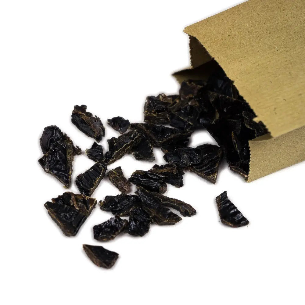 Dried black herbs spilling from a brown paper bag, showcasing natural ingredients for culinary use.