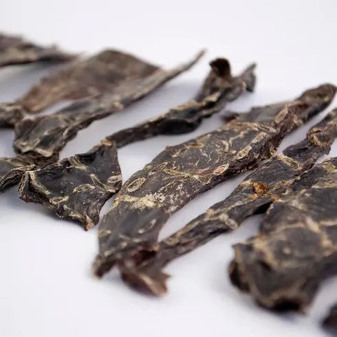 Dried beef jerky strips arranged neatly on a white background, showcasing texture and color.