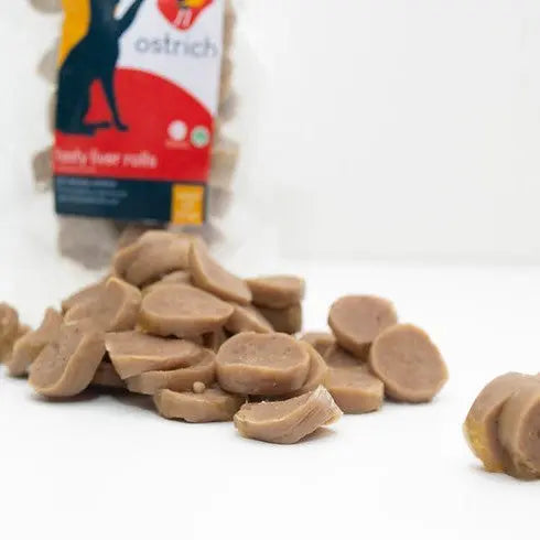 Ostrich-flavored pet treats in a bag, with sliced pieces scattered on a white surface.