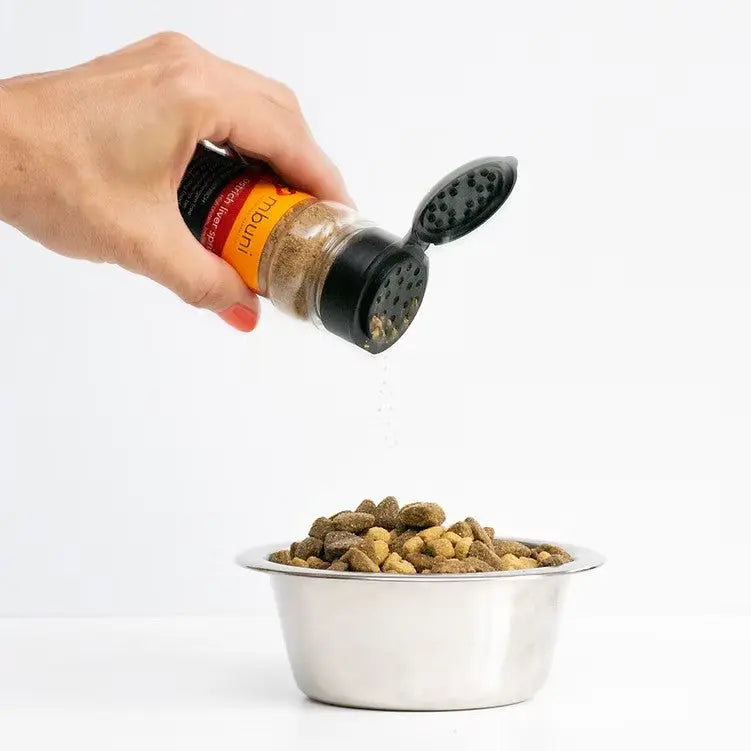 Hand pouring seasoning from a bottle onto a bowl of pet food.