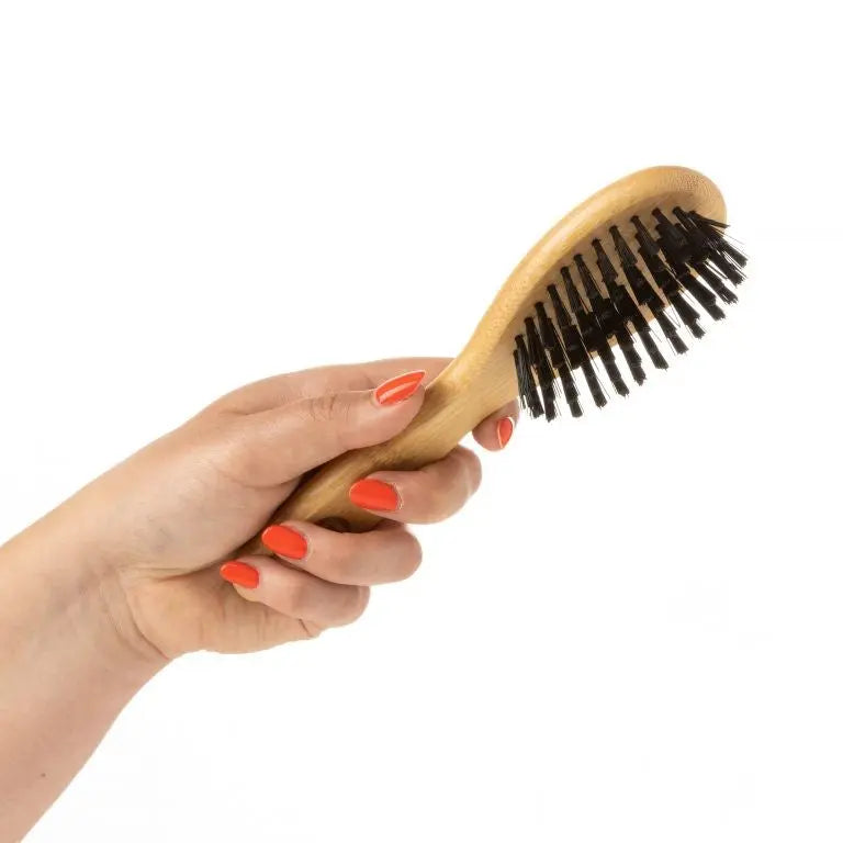 Hand holding a wooden hairbrush with black bristles against a white background.