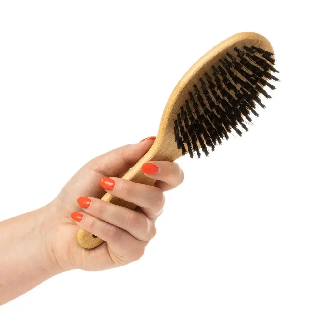 Hand holding a wooden hairbrush with bristles, perfect for detangling and styling hair.