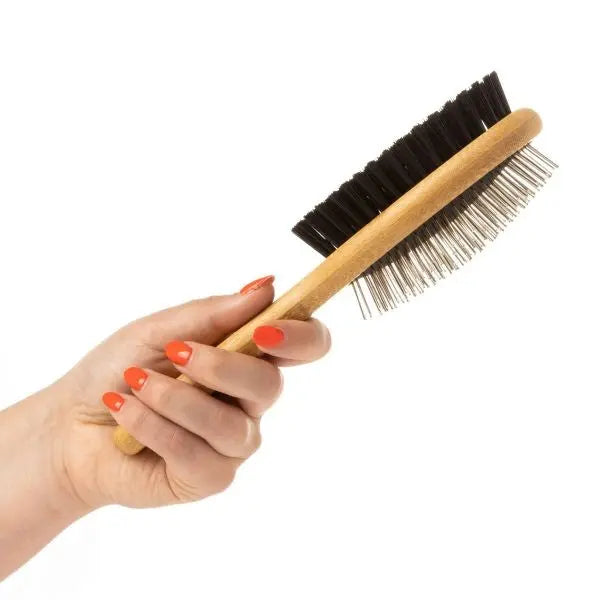 Hand holding a wooden hairbrush with bristles and metal pins for styling and grooming hair.