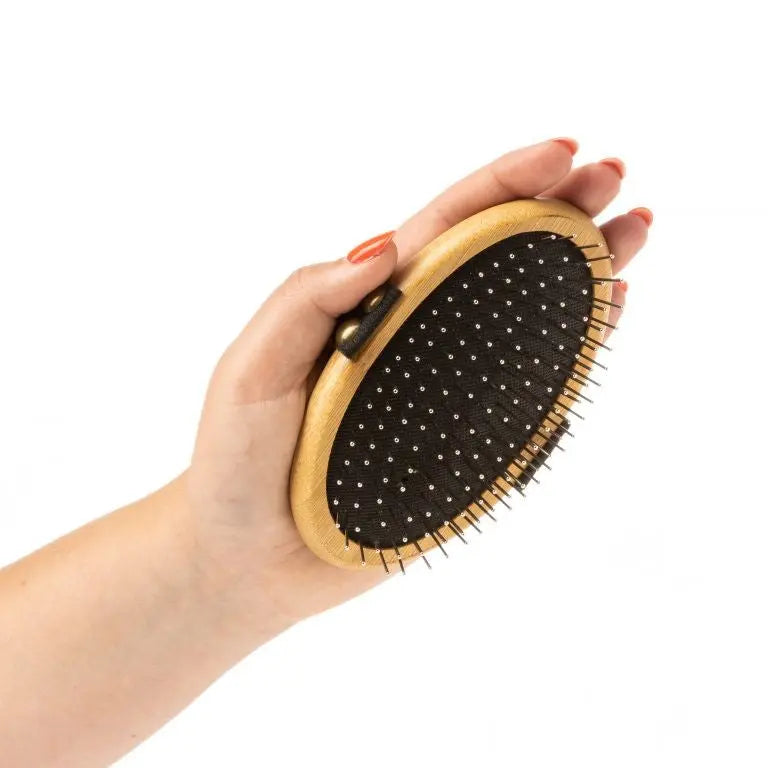 Hand holding a wooden hairbrush with rounded pins for gentle detangling and styling.