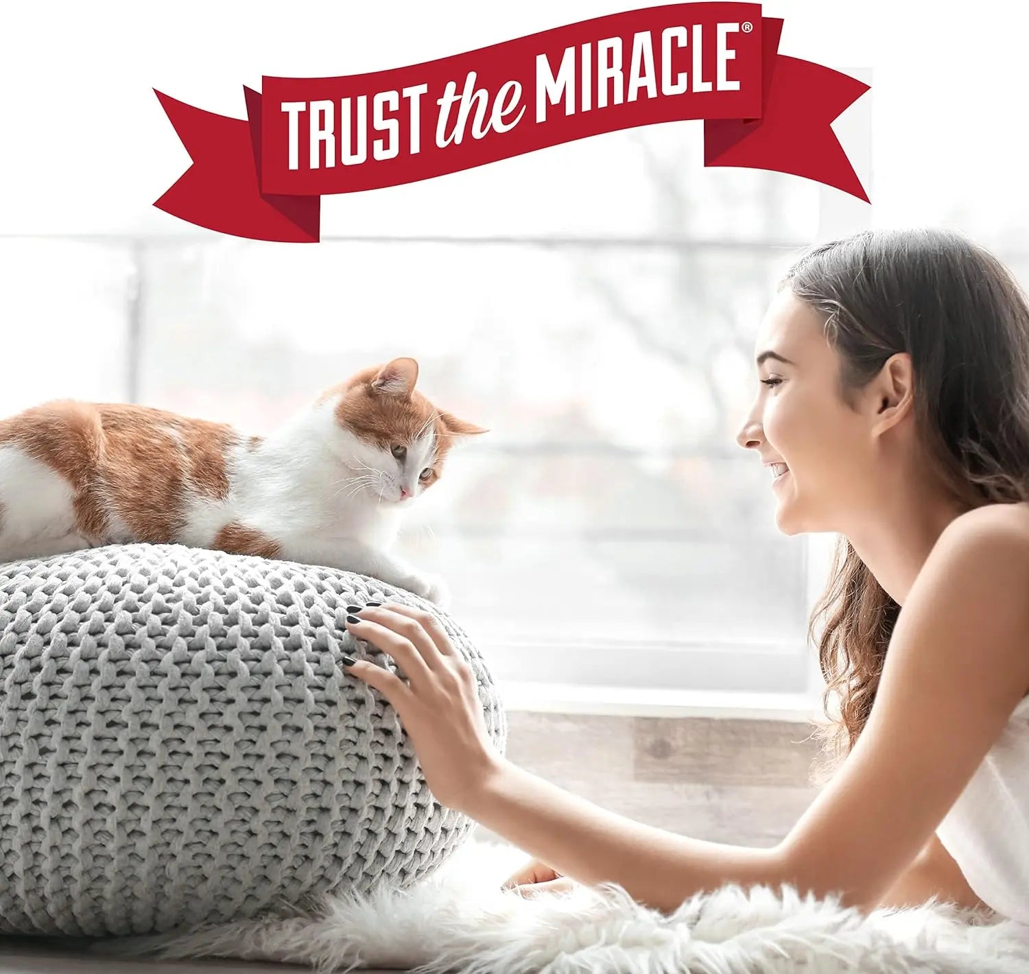 Woman smiling at a cat on a cozy cushion, promoting pet companionship and comfort.