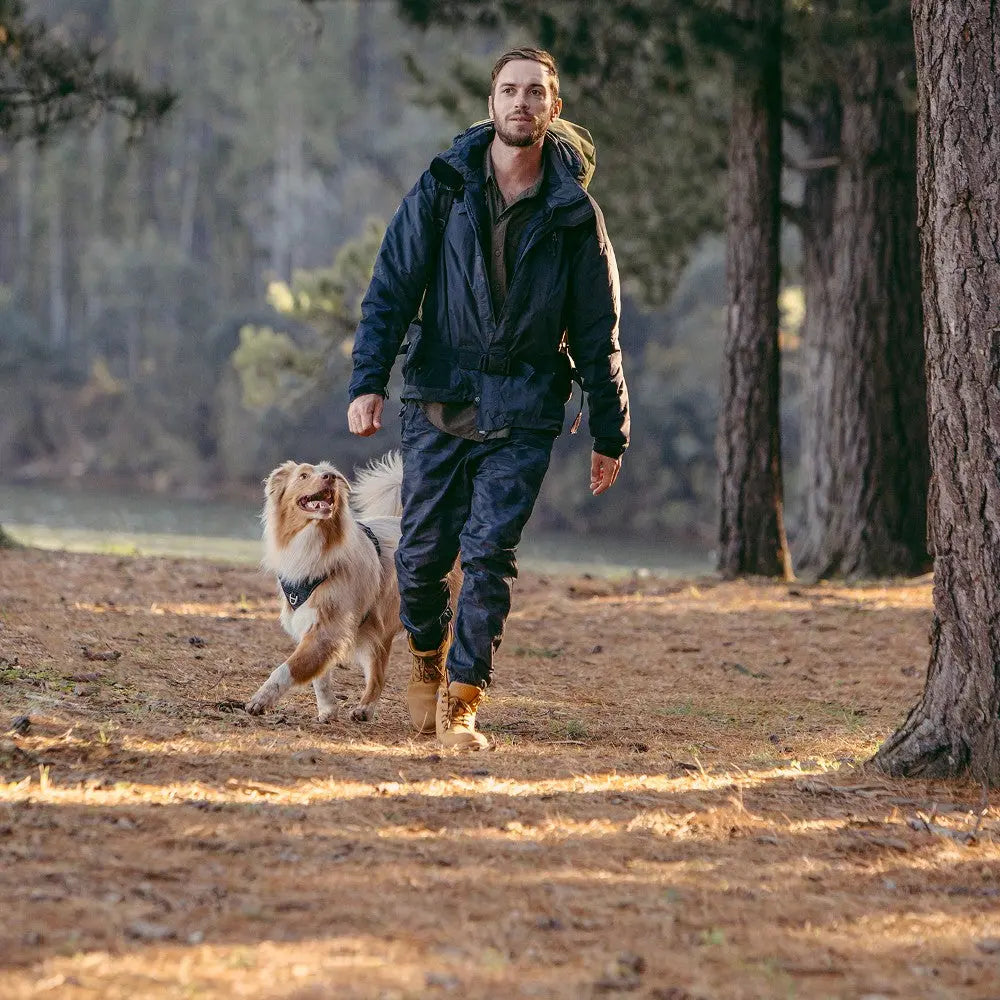 Man walking a dog in a forest, showcasing outdoor adventure and companionship.