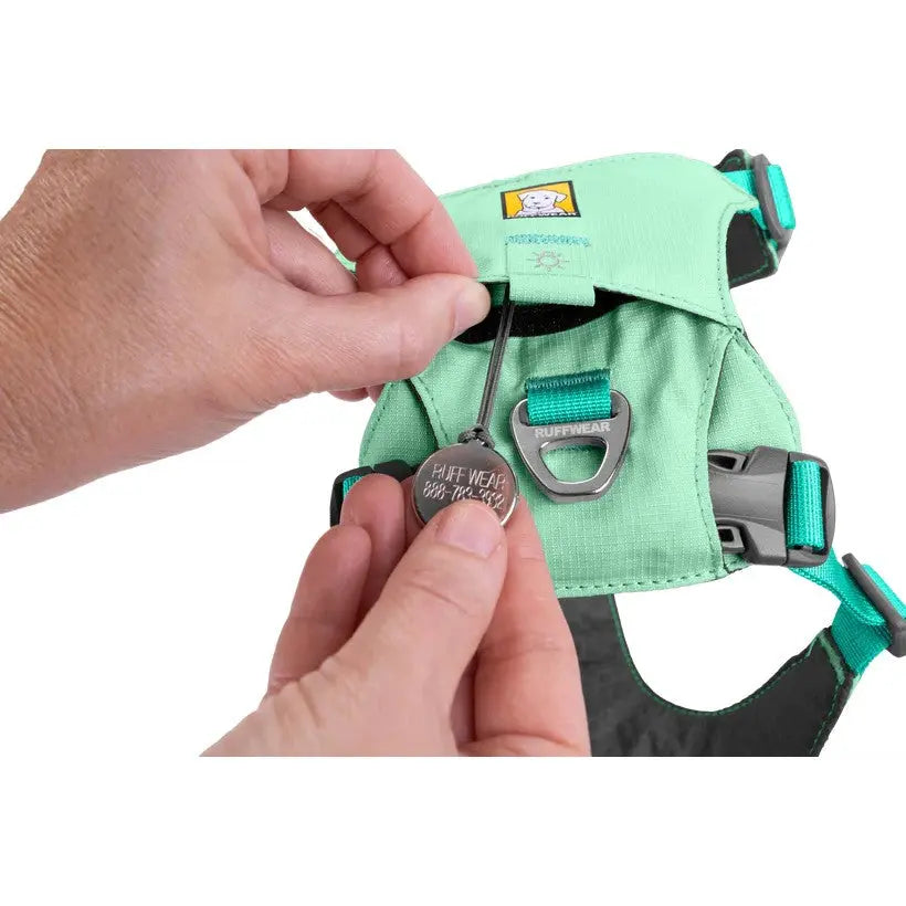 Hand adjusting a pet harness with a tag, showcasing its durable design and secure fit.