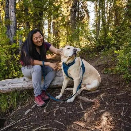 Woman enjoying a hike with her dog in a lush forest setting.