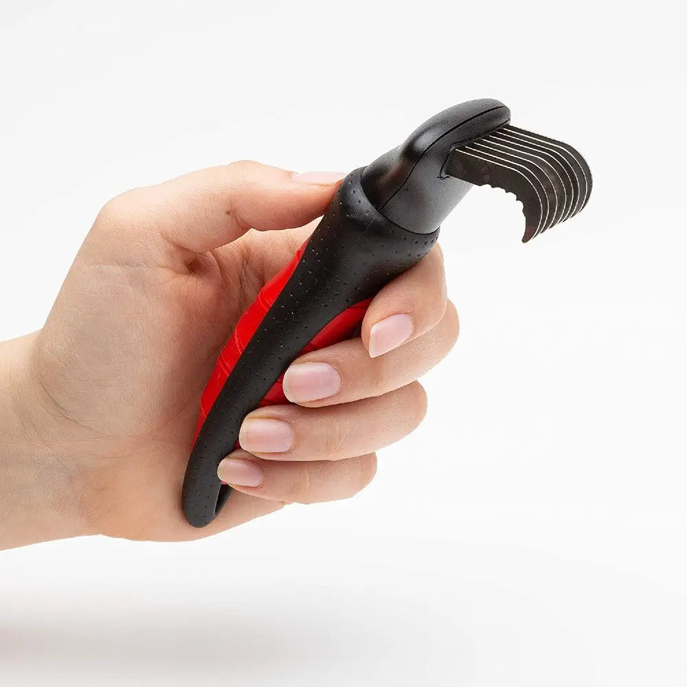 Hand holding a red and black ergonomic tool with curved metal prongs for efficient scraping or grooming.