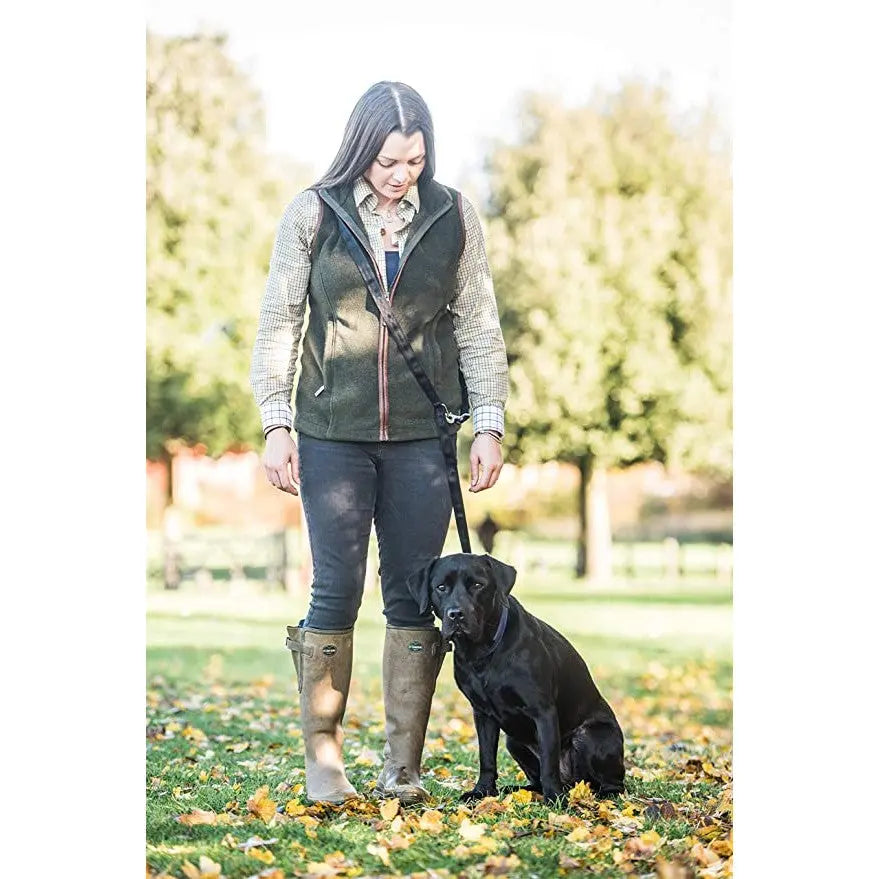 Woman walking a black Labrador in a park with autumn leaves, wearing a stylish outdoor outfit.