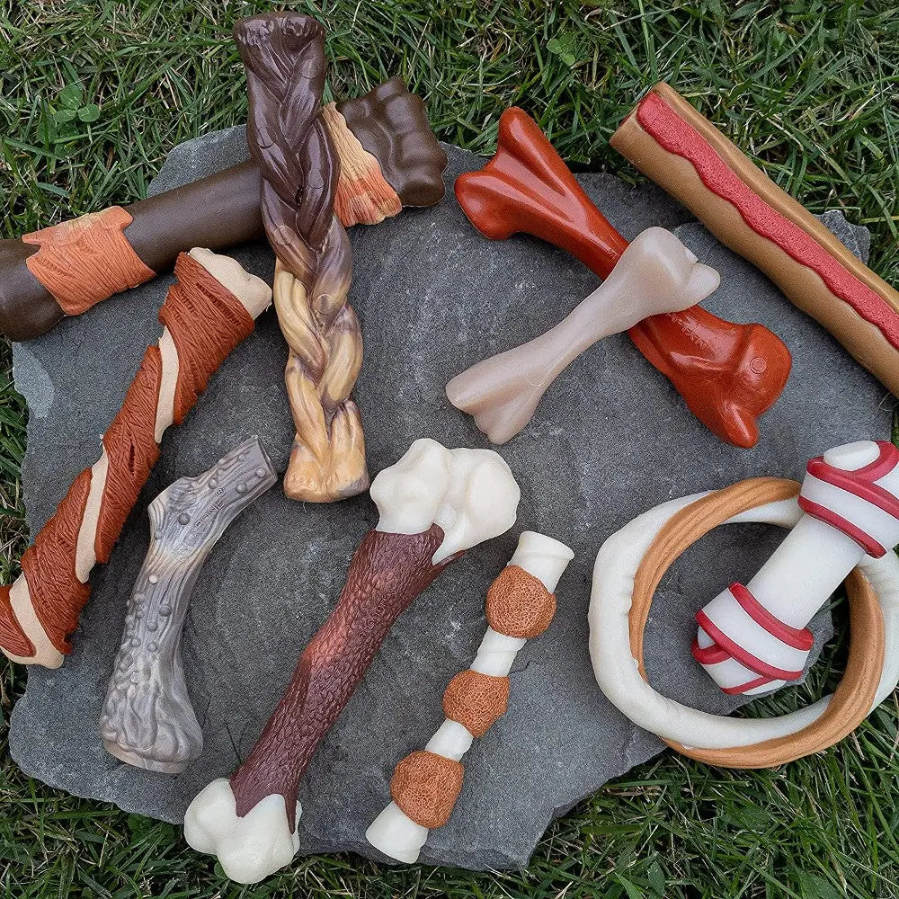 Assorted dog chew toys in various shapes and textures on a stone surface.