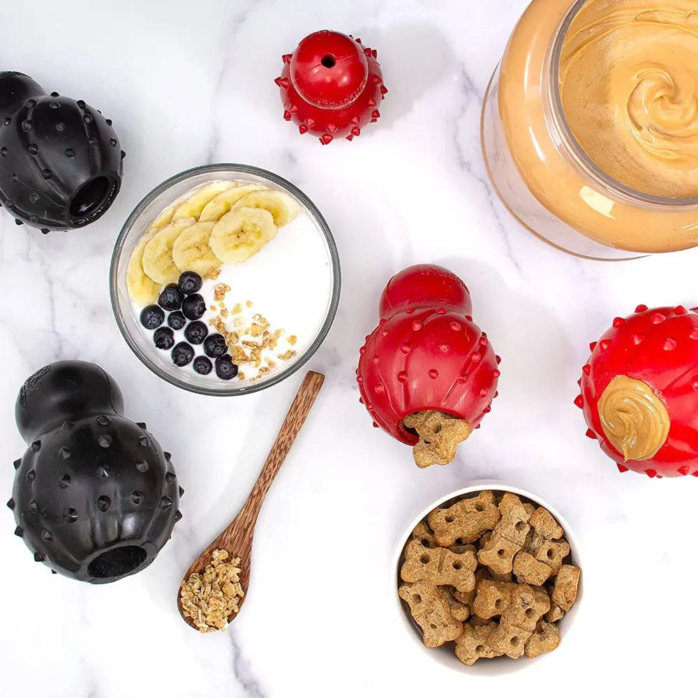 Dog treat preparation with KONG toys, yogurt, fruit, and peanut butter on a marble surface.