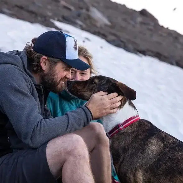 Man and woman enjoying time with a dog in a snowy outdoor setting.