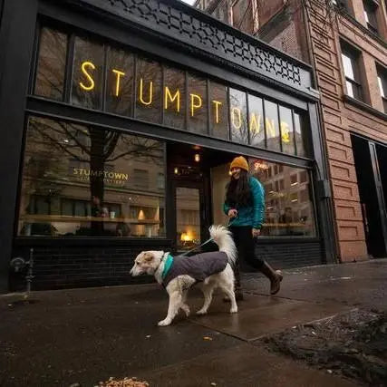 Person walking a dog outside Stumptown coffee shop in a city setting.
