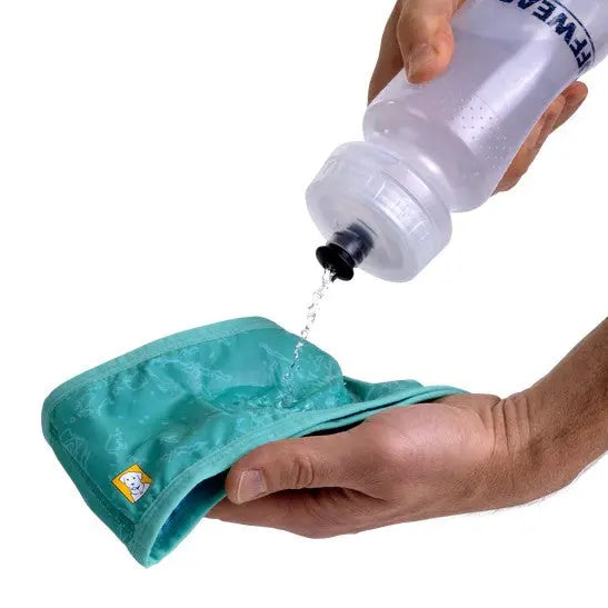 Hand pouring water from a bottle onto a teal pet training pad for easy cleaning and maintenance.
